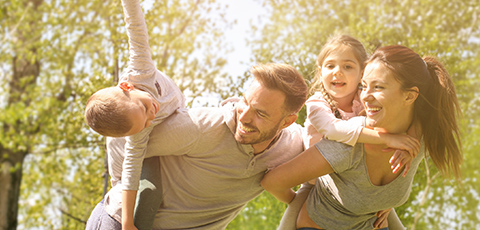 Smiling parents piggybacking their kids during a sunny day in the park - https://www.auburninsurance.org