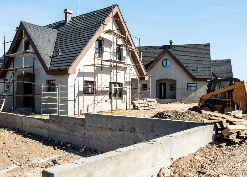 A house under construction with a yellow bulldozer parked nearby, surrounded by construction materials and debris.